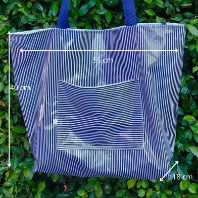 Saco azul às riscas com bolso frontal e alças, pendurado em folhagem verde