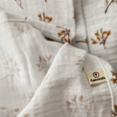 Pano branco com padrão de ramos castanhos e verdes e etiqueta cusnitos