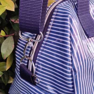 Mala azul com riscas brancas e alça larga azul escura junto a folhagem verde