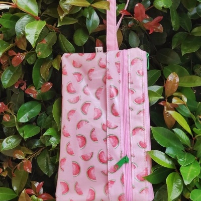 Bolsa cor de rosa com padrão de fatias de melancia pendurada em folhas verdes