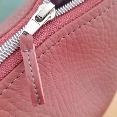 Fecho de correr prateado em carteira ou bolsa rosa de couro sintético.