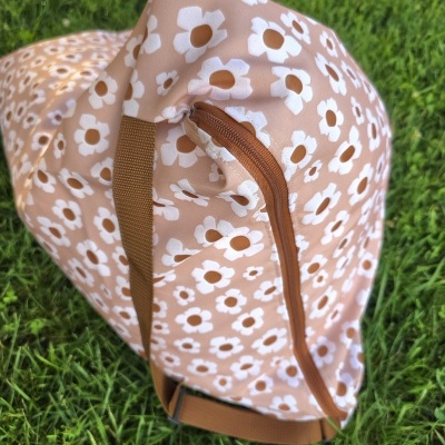 Mala saco rosa com flores brancas e castanhas sobre relva verde