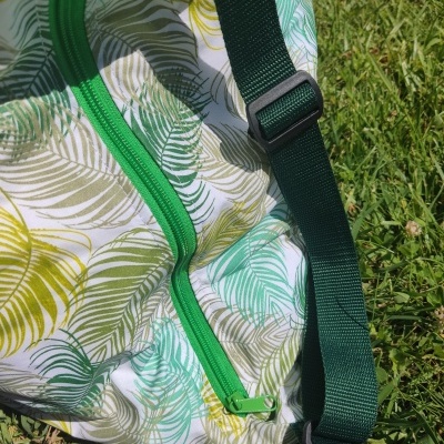Mala ou mochila com padrão de folhas coloridas e alça verde escuro sobre relva