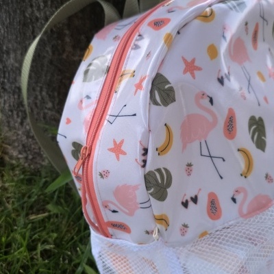 Mochila branca com padrão colorido e bolso de rede encostada a árvore