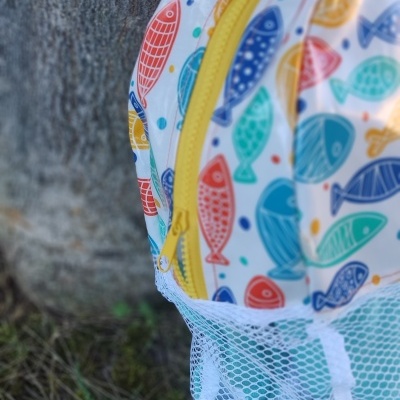 Mochila colorida com padrão de peixes e bolso de rede encostada a uma árvore
