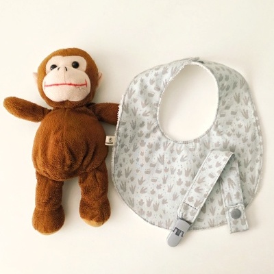 Boneco de peluche castanho e babete cinzento com padrão ao lado