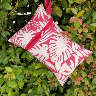 Mala de mão vermelha com padrão branco pendurada em sebe verde