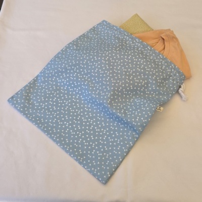 Saco azul com padrão de triângulos brancos e cordão, contendo duas t-shirts dobradas, sobre superfície branca.