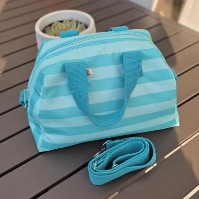 Mala azul com riscas horizontais e alça removível sobre mesa castanha com vaso branco e planta suculenta