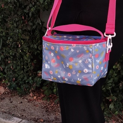 Bolsa térmica azul com flores e alças rosa num cenário exterior