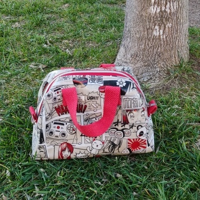 Bolsa de mão pequena com padrão gráfico colorido e alças vermelhas sobre relva junto a árvore