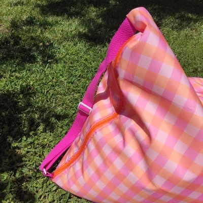 Mala xadrez rosa e laranja com alça rosa sobre relva