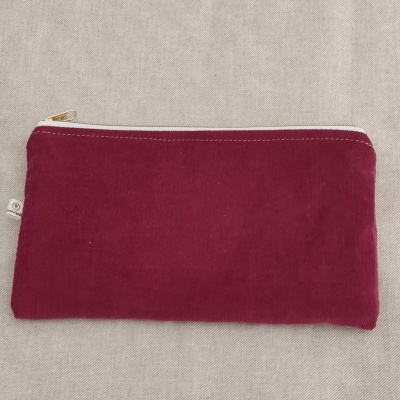 Estojo retangular em veludo vinho com fecho branco sobre tecido cinza