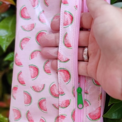 Bolsa rosa com padrão de melancia e fecho verde segurada por mão com unhas vermelhas