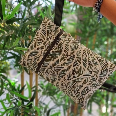 Bolsa de tecido com padrão folhas verdes e bege, alça preta, segurada por mão com pulseiras