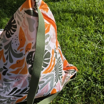 Mala saco com padrão floral colorido e alça verde na relva