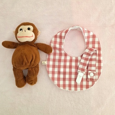 Boneco de peluche macaco e babete xadrez branco e vermelho em superfície rosa