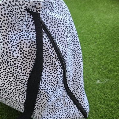 Mala branca com manchas pretas e fecho zip preto sobre relva artificial verde