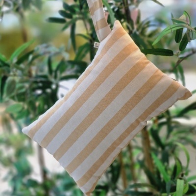 Almofada riscada branca e bege com alça, segurada por mão com pulseira, plantas ao fundo