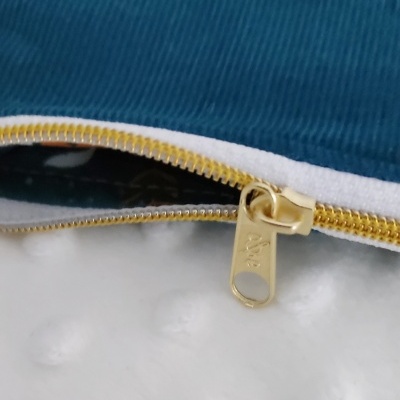 Fecho dourado YKK em tecido azul com borda branca, sobre tecido branco com pontos em relevo