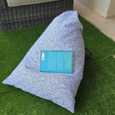 Pufe triangular com padrão de bolinhas pretas em fundo branco sobre relva artificial