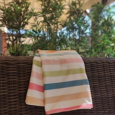 Manta com riscas coloridas pendurada em sofá de vime num espaço exterior com plantas