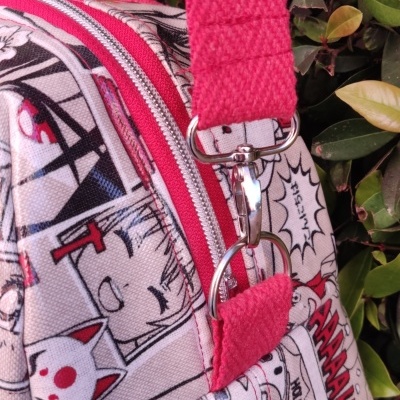 Mala com padrão de banda desenhada e detalhes rosa sobre fundo de folhas verdes