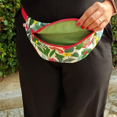 Bolsa pochete colorida com padrão de folhas e interior verde com pontos brancos.