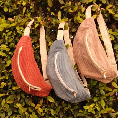 Três malas tipo pochete de veludo cotelê coloridas penduradas numa sebe