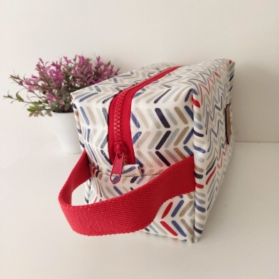 Necessaire colorida com padrão geométrico e fecho vermelho, com planta ao fundo