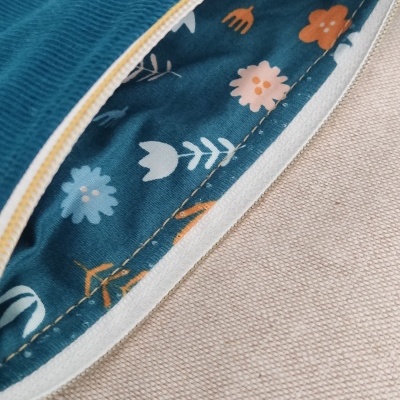 Estojo azul de veludo com interior floral e fecho amarelo sobre tecido bege