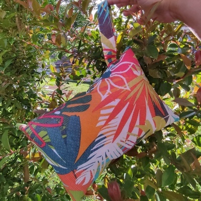 Bolsa pequena de tecido colorida com padrão tropical segurada à frente de árvore