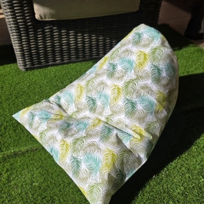 Puff estampado com padrão de folhas em frente a cadeira de vime com almofada