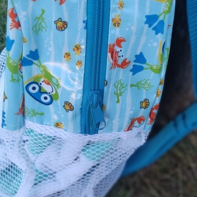 Mochila infantil azul claro com padrão colorido e bolso de rede branco