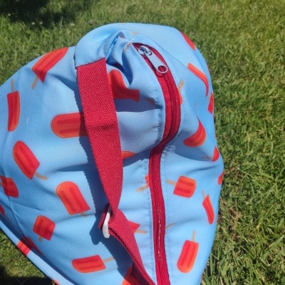 Mochila azul com padrão de gelados vermelhos e fecho vermelho na relva