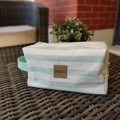 Necessaire riscada verde clara e branca com etiqueta na mesa de vime