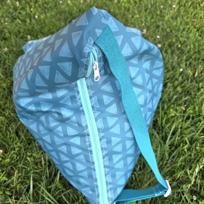 Bolsa azul com padrão de triângulos e alça azul sobre relva verde