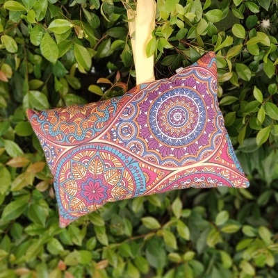 Almofada retangular colorida com padrão mandala pendurada entre folhas verdes