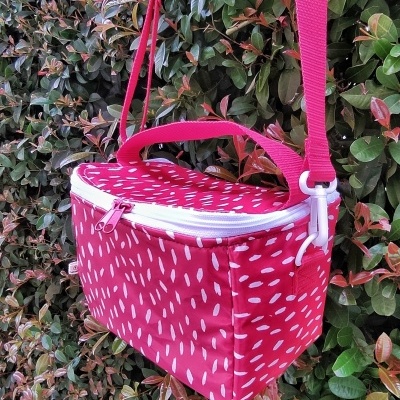 Mala pequena vermelha com manchas brancas e alça ajustável suspensa numa sebe