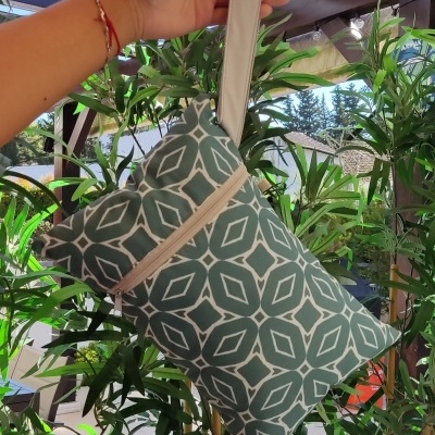 Mala de mão cinza com padrão geométrico branca e pega bege suspensa por uma mão