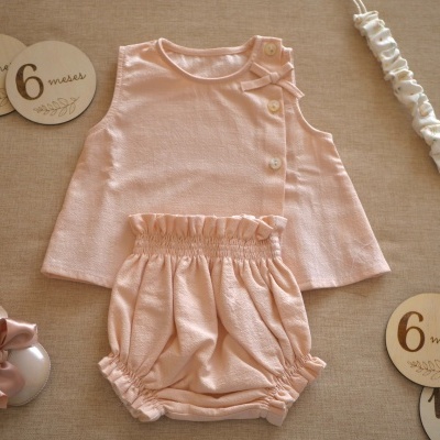 Conjunto de bebé em tecido cor-de-rosa com botões e laço, sapatos cor-de-rosa e discos de madeira com idades