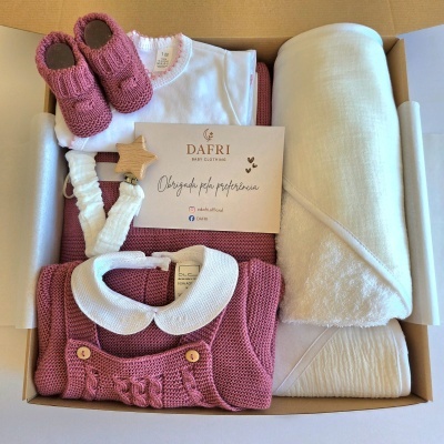 Vista superior de caixa com roupa de bebé em lã cor rosa velho, botins, manta creme e cartão da marca DAFRI