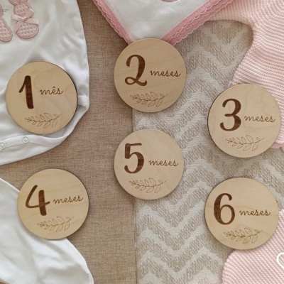 Seis placas de madeira com meses gravados sobre tecidos e roupa de bebé