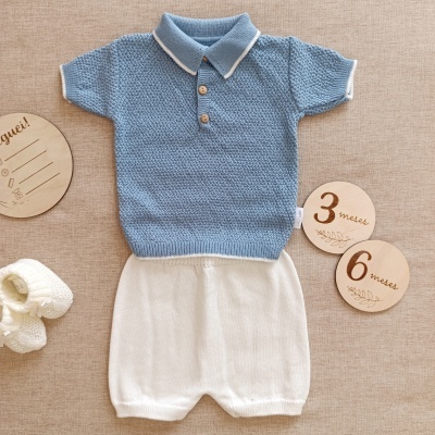 Conjunto bebé com camisola azul de malha, calças brancas, sapatinhos de lã e placas de madeira