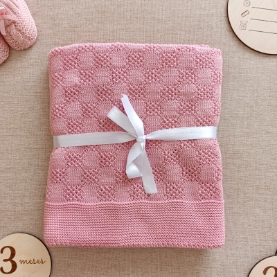 Manta tricotada cor-de-rosa com fita branca sobre superfície bege