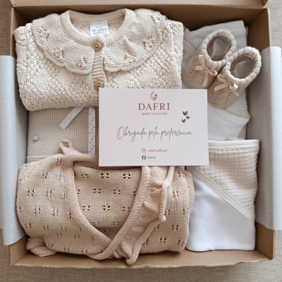 Conjunto de roupa de bebé em malha bege e mantas brancas numa caixa de cartão