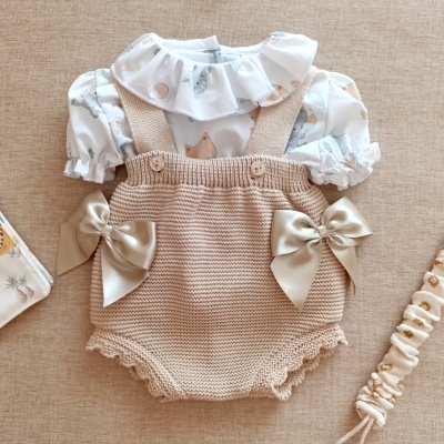 Conjunto de roupa de bebé com body branco estampado e jardineira de malha bege com laços