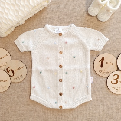 Body de bebé branco com botões e pompons coloridos, mantinha, sapatinhos e discos de madeira com meses em português