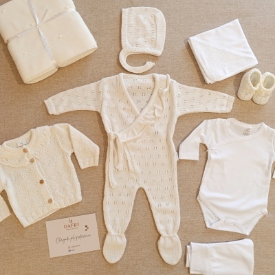 Conjunto de roupa de bebé branca e creme com cartão DAFRI sobre fundo bege.
