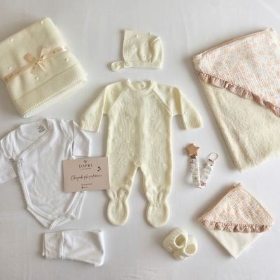 Conjunto de bebé com roupa de malha creme e branca, mantas, e porta-chupetas com detalhe de estrela de madeira